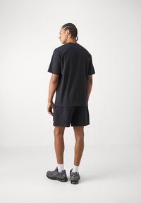 Black short-sleeve t-shirt and shorts outfit, made of cotton, with a relaxed fit and paired with gray athletic shoes and white socks.