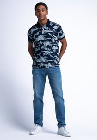 Námořnická polo košile se světle zeleným květinovým vzorem, krátké rukávy a límec na knoflíky. V kombinaci se světle modrými džíny a bílými teniskami.