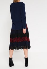 Blusa azul marino de mangas largas, combinada con una falda de encaje que presenta rayas horizontales en negro, rojo y azul marino. Botines negros completan el look.