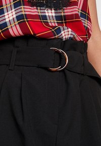 Pantalones negros de cintura alta con frente plano, que cuentan con un cinturón de hebilla metálica circular. Tejido texturizado con detalles cosidos y bolsillo lateral.