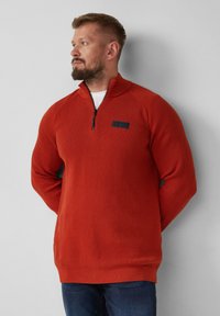 Roter Zip-Up-Pullover mit strukturiertem Strickmuster, ausgestattet mit einem schwarzen Logopatch auf der Brust sowie gerippten Bündchen und Saum.