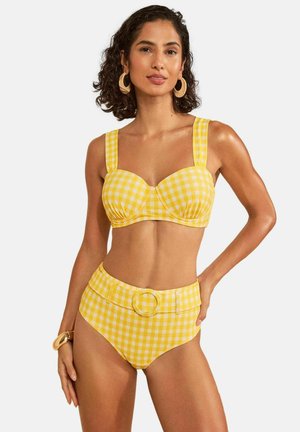Frau trägt gelb-weißen karierten High-Waist-Bikini mit Schnallengürtel, passendem Oberteil mit breiten Trägern, großen Creolen und Armband.