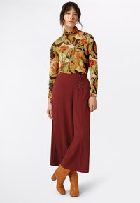 Un col roulé floral multicolore à manches longues associé à un pantalon large bordeaux taille haute avec des boutons décoratifs et des bottines.