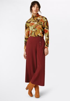 Langärmliger, mehrfarbiger Blumenrollkragenpullover kombiniert mit hochtaillierten weinroten, weiten Hosen mit dekorativen Knöpfen und Ankle-Boots.