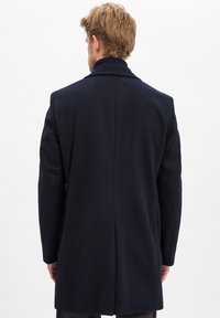Granatowy wełniany płaszcz z pojedynczym rozcięciem, klapami w kształcie litery notch i dopasowanym krojem, widziany z tyłu. Gładka tekstura bez widocznych wzorów.