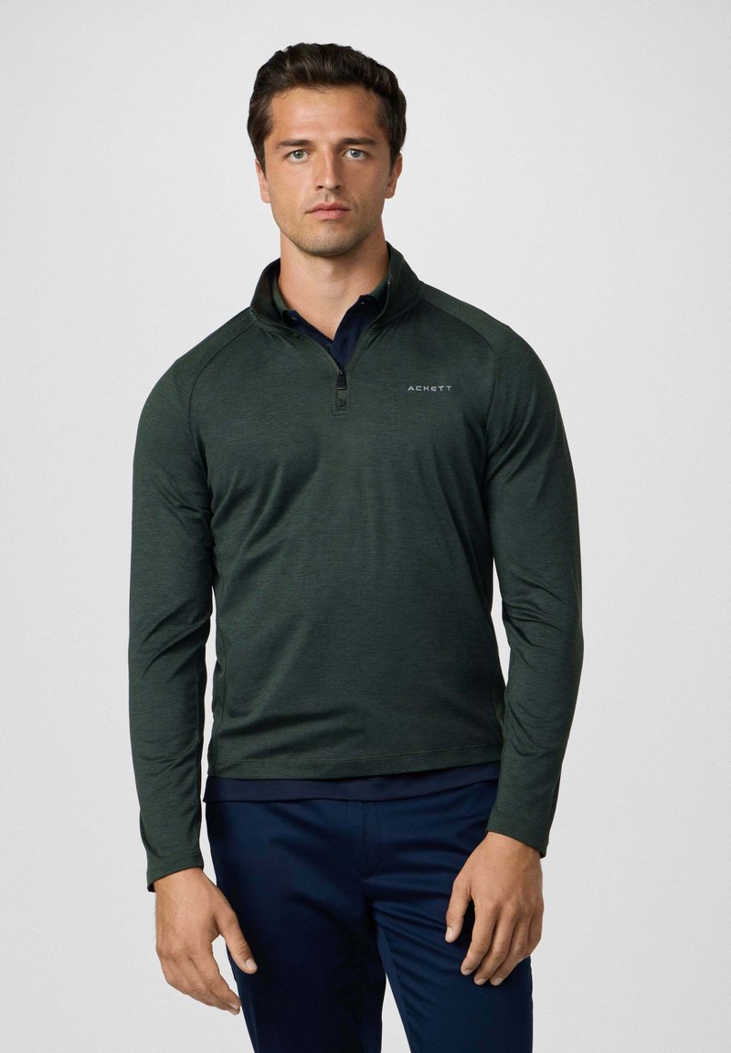 Pullover lungo a maniche lunghe verde scuro con colletto alto e mezza zip, caratterizzato da un design aderente e un logo bianco sul petto.
