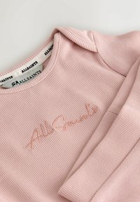 Svetloružový rebrovaný sweatshirt s okrúhlym výstrihom. Obsahuje jemne vyšívané logo v ladiacej farbe. Mäkká textúra a priliehavé rukávy.