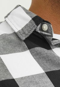 Collar de camisa a cuadros en blanco y negro, con cierre de botón. La tela tiene un tejido texturizado con bloques de color alternos bien definidos.