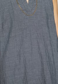 Robe bleu foncé avec un col en V, en tissu texturé présentant des rayures horizontales subtiles. Elle offre une silhouette simple et élégante.