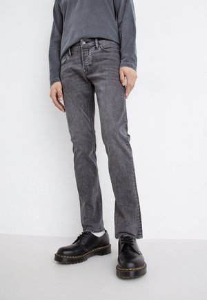 Graue Denim-Jeans mit geradem Bein, ausgestattet mit Fronttaschen und dezenten Nähten. Kombiniert mit schwarzen Schnürschuhen und einem dunklen Oberteil.