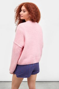 Pulover roz supradimensionat, cu o textură moale și tiv cu nervuri, asortat cu pantaloni scurți în dungi albastre și roșii. Modelul este văzut din spate.