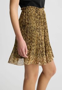 Gonna mini plissettata in tessuto leggero e semi-trasparente, con stampa leopardata in tonalità di marrone e beige, dotata di vita elasticizzata.