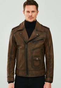 Veste de moto en cuir brun avec fermeture éclair à l'avant, poches latérales et épaulettes. Présente une texture légèrement usée et une coupe ajustée.