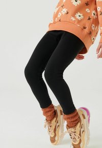 Svarta leggings i elastiskt material, kombinerade med bruna strumpor och klumpiga sneakers med nyanser av beige och rosa accent.
