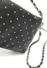 Sac en cuir noir ornés de clous argentés, d'une forme triangulaire et d'une chaîne en bandoulière avec des accents en cuir. Surface texturée et détails métalliques visibles.