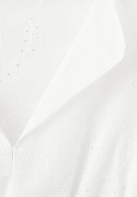 Tissu blanc à œillets avec broderie florale présentant un col pointu et une ouverture en V.
