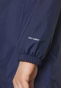 Granatowa wodoodporna kurtka z elastycznymi mankietami; na przodzie logo "DRY VENT" w białym kolorze. Gładka, teksturowana tkanina; lekka konstrukcja.