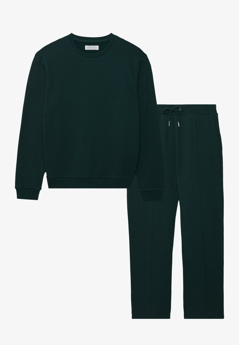 Maglietta a maniche lunghe di un verde scuro a coste con colletto girocollo e pantaloni coordinati con cordino. Entrambi hanno una consistenza morbida e una vestibilità comoda.