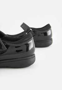 Schwarze lacklederne Schuhe mit glatter Oberfläche, elastischen Bändern für eine gute Passform und erhöhten schwarzen Gummisohlen, die für Komfort ausgelegt sind.