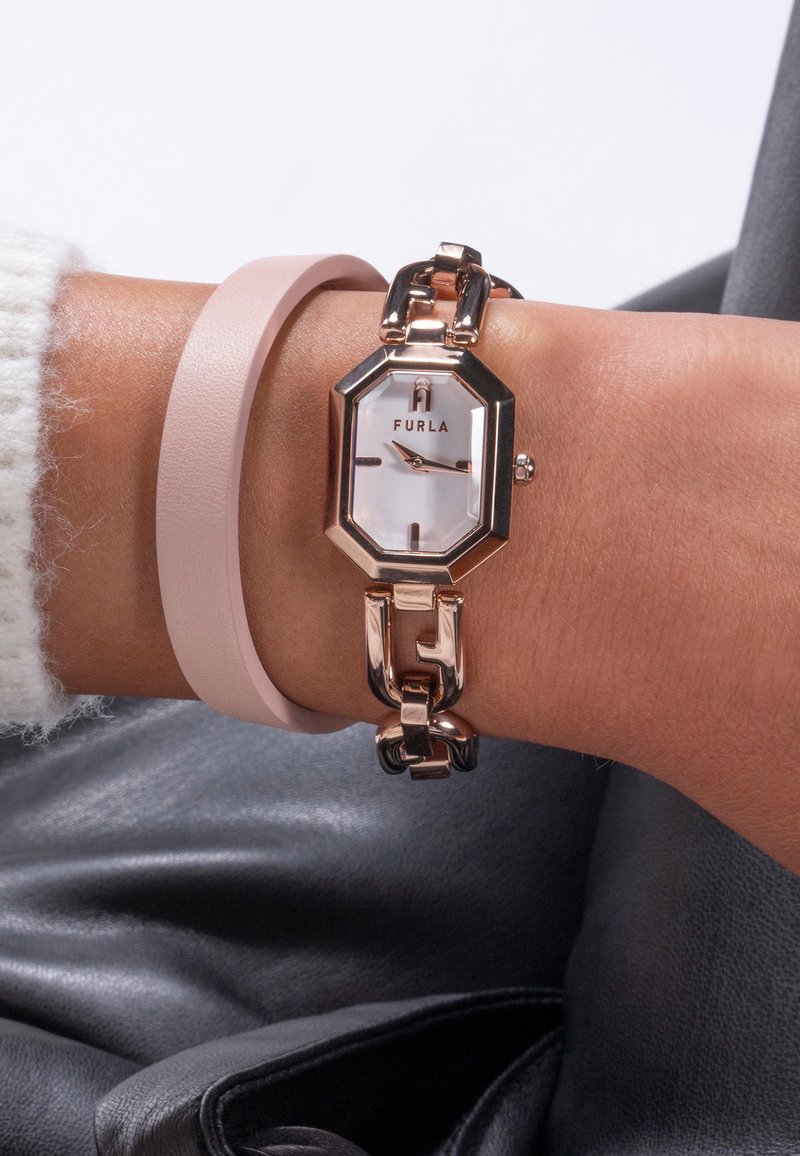 Orologio ottagonale in oro rosa con quadrante bianco, dotato di bracciale a maglie. Abbinato a un cinturino in pelle rosa liscia al polso.