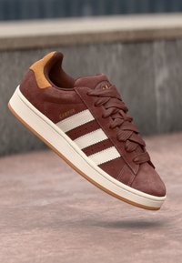 Brune ruskind sneakers med tre hvide striber, en tekstureret mellemsål og brune detaljer på hælen og tungen. Guld "CAMPUS" bogstaver inkluderet.