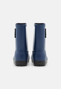 Bottes de pluie en caoutchouc bleu avec une texture lisse, une tige courte et des semelles noires. Présentent une petite sangle de chaque côté pour un enfilage facile.