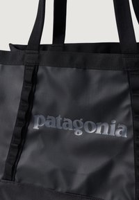 Geantă de umăr neagră, fabricată dintr-un material durabil, cu un logo "patagonia" lucios. Dispune de mânere plate și rezistente și o suprafață texturată.