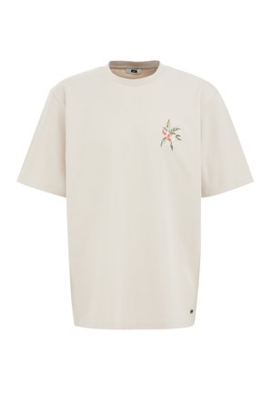 Beżowy T-shirt z krótkim rękawem wykonany z bawełny. Ma mały kwiatowy nadruk na lewej piersi oraz akcent z logo w pobliżu dołu.