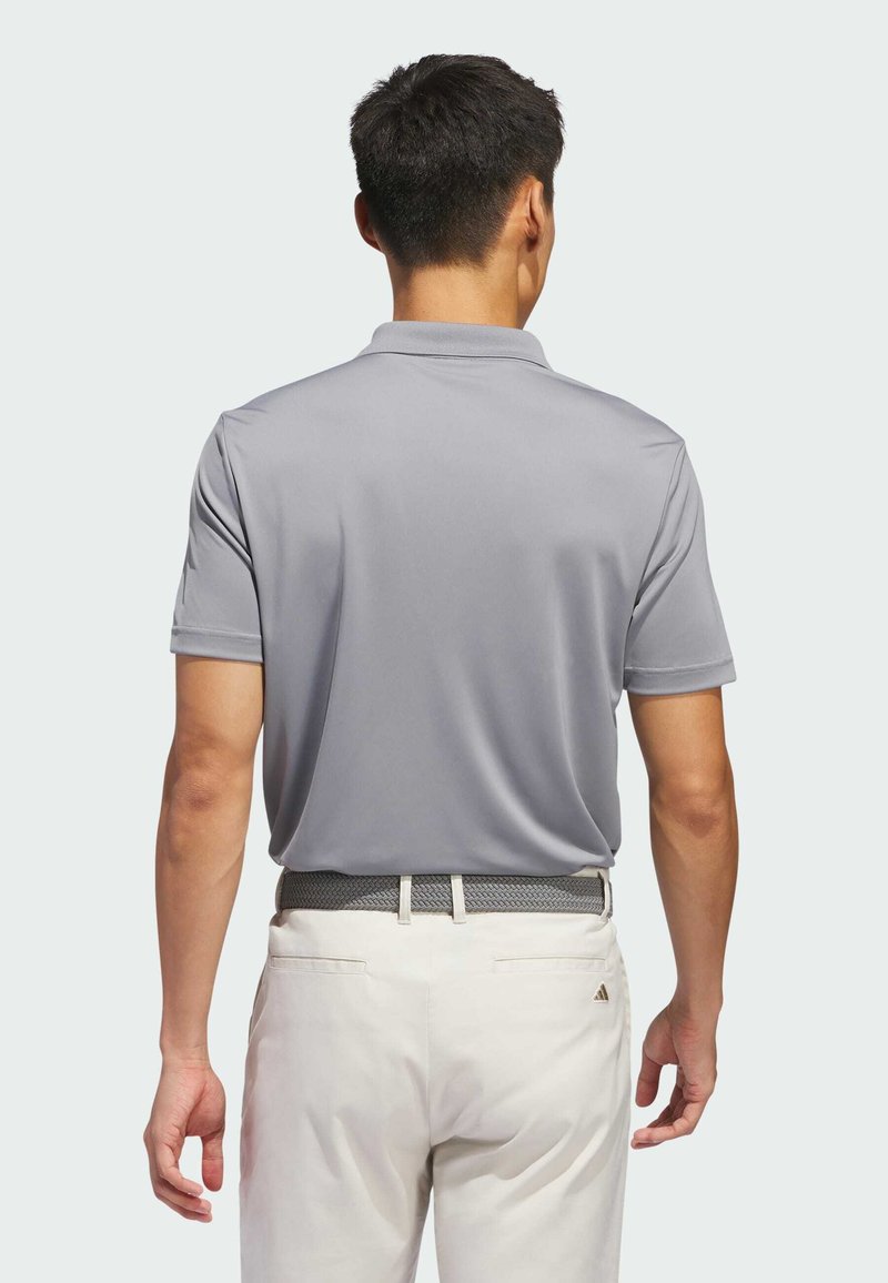 Polo gris à manches courtes, en tissu lisse, avec un col classique ; porté avec un pantalon clair et une ceinture tissée.