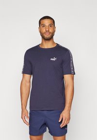 T-maica navy modre barve s kratkimi rokavi, izdelana iz mehkega blaga in z okroglim izrezom. Ima logotip Puma in patterned poudarke na ramenih.