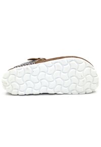 Chaussure en cuir brun avec un design supérieur texturé, équipée d'une semelle en caoutchouc blanche avec un motif ondulé, des coutures visibles et une fermeture à sangle.