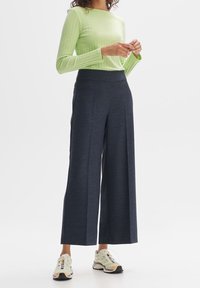 Haut à manches longues côtelé vert clair associé à un pantalon large bleu marine foncé. Les baskets présentent des accents beiges et noirs.