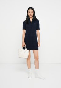 Ναυτικός πλεκτός φόρεμα με κοντά μανίκια, κολάρο με φερμουάρ και ραβδωτή υφή. Συνδυασμένο με μια μικρή λευκή τσάντα και λευκά αθλητικά παπούτσια.