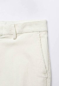 Gros plan de la taille d’un pantalon en velours côtelé couleur crème avec passants de ceinture et poche latérale visibles.