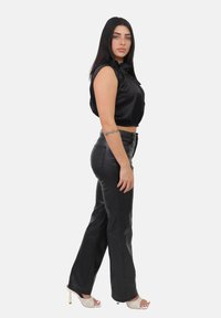 Zwarte satijnen crop top met opgeblazen schouders, gecombineerd met zwarte, hooggetailleerde nep leren broek. Schoeisel met lichtgekleurde, open teen hakken.