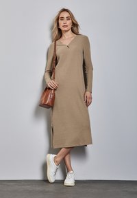 Abito beige a maniche lunghe e righe, con scollatura a V e uno spacco laterale, abbinato a sneaker bianche e una borsa a tracolla marrone.