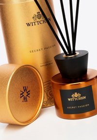 Dyfuzor Wittchen Secret Passion charakteryzuje się cylindrycznym złotym opakowaniem, bursztynową szklaną butelką z czarną nakrętką oraz czarnymi pałeczkami reed.