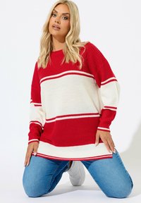 Punainen ja valkoinen raidoitettu ylisuurikokoinen neulepaita, jossa on pitkät hihat, ribattu kaula-aukko ja helma. Yhdistetty sinisiin farkkuihin ja valkoisiin lenkkitossuihin.