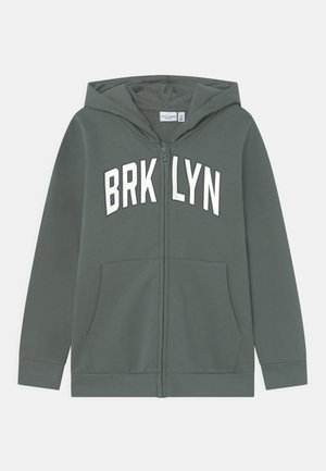 Felpa verde con zip e stampa bianca "BRKLYN" sul petto. Presenta un cappuccio e tasche frontali. Tessuto liscio, polsini a costine.