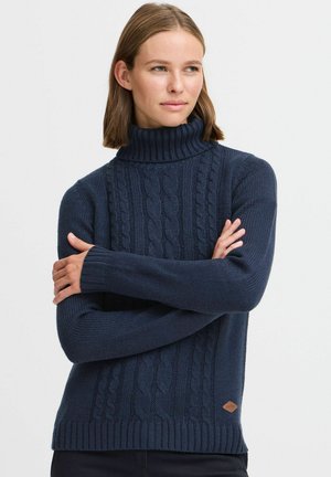 Pull en maille bleu marine à col roulé avec des motifs en torsades et des poignets côtelés. Présente un patch en cuir avec logo au bas. Tissu texturé, apparence chaleureuse.