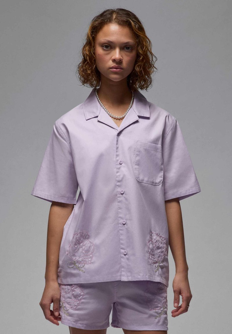 Camicetta a maniche corte color lavanda e pantaloni corti abbinati, realizzati in tessuto morbido, con motivi floreali ricamati in rosa su entrambi i lati.