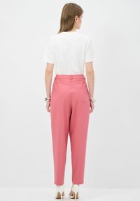 Witte katoenen t-shirt met korte mouwen, gecombineerd met hooggenaaide, op maat gemaakte roze broek met een subtiele achterzakdetails en een zachte textuur.