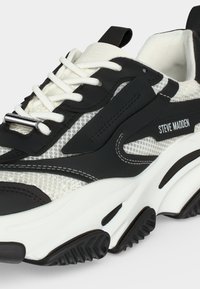 Close-up van een zwart-witte Steve Madden sneaker met witte veters, een gestructureerde mesh bovenzijde en een dikke, patroonzool.