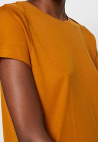 T-shirt a maniche corte con collo rotondo di un giallo senape solido. Realizzato in tessuto liscio e leggero con una vestibilità sagomata e dettagli di cucitura minimi.