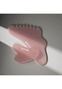Deux outils de massage en silicone rose avec le logo « ZOË AYLA », l’un en forme de pied avec des rainures pour les orteils, l’autre en forme de cœur, sur une surface grise.