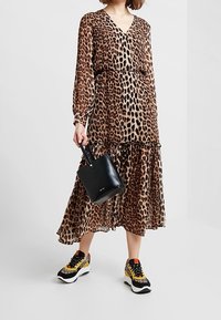 Kleid mit Leopardenmuster, langen Ärmeln, V-Ausschnitt, elastischem Bund und schichteter Rock, kombiniert mit einer schwarzen Handtasche und mehrfarbigen Sport-Sneakern.