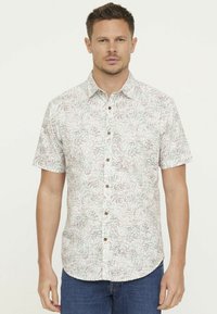 Chemise à manches courtes avec boutonnière de couleur beige clair ornée d'un motif de feuilles vertes et brunes. Comprend des boutons bruns et un col.