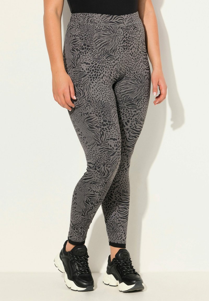 Leggings gris avec un motif animalier abstrait, taille haute et texture douce, associés à des chaussures de sport noires.