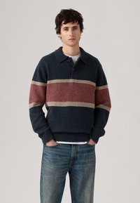 Knitted navy sweater with a red and cream horizontal stripe, featuring a collar, two buttons, and ribbed cuffs and hem. Casual fit.