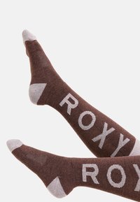 Brązowe skarpetki z białymi akcentami na palcach i pięcie, z dużym nadrukiem "ROXY" po bokach, wykonane z teksturowanego materiału dzianinowego.